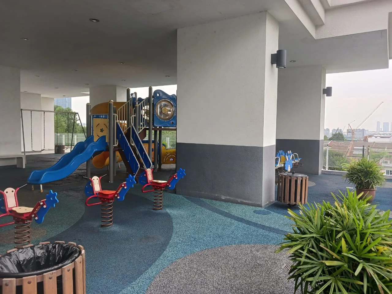 Exterior type: children's playground; features: playground equipment with slides and climbing structures, spring riders in the shape of animals, swing set, rubberized flooring, planters with greenery, trash bin, open space with city view; style: modern.